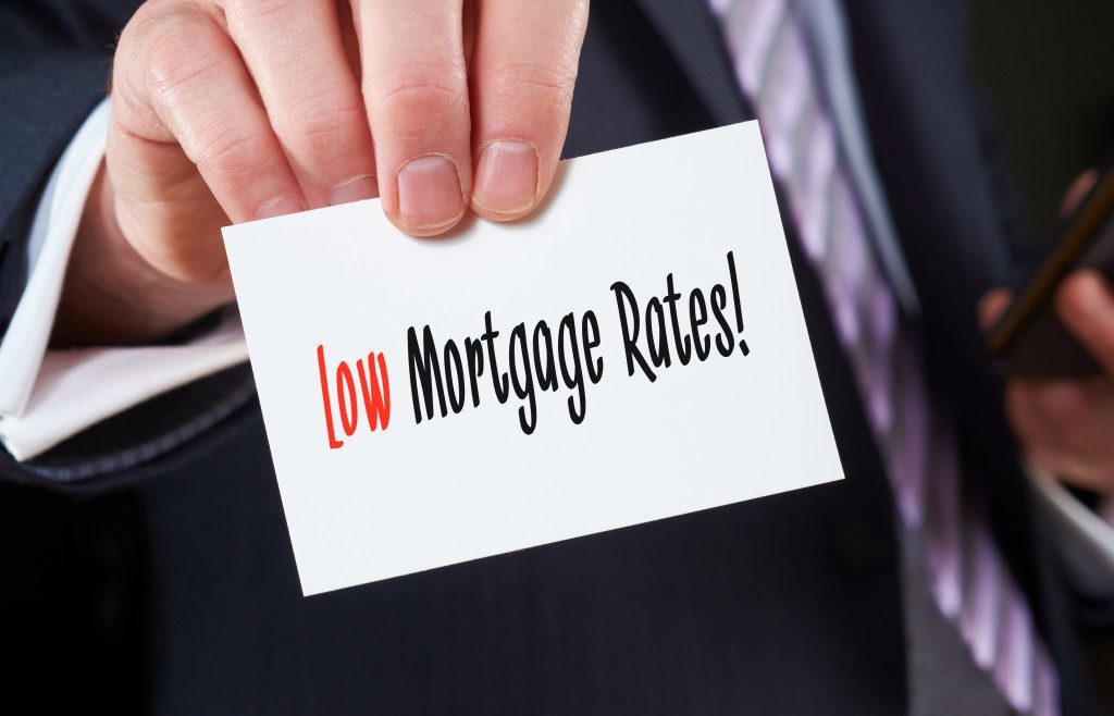 A businessman holding a business card with the words, Low Mortgage Rates, written on it.