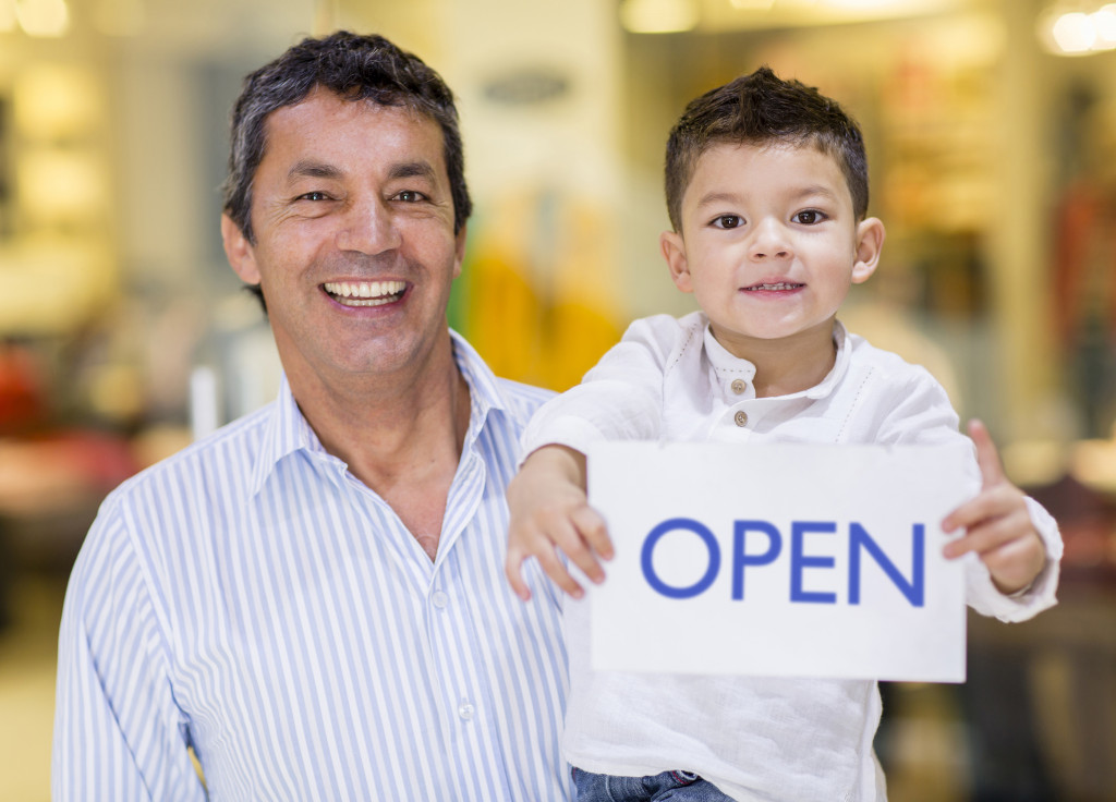 father and son holding open sign